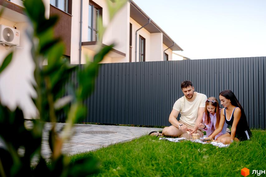 Котеджне містечко КМ WEST TOWN XIV. Сім'я з двох дітей відпочиває на галявині біля будинку.