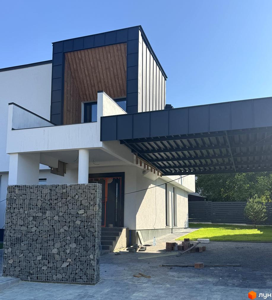 Котеджне містечко КМ Lake House Sokilnyky. Зовнішній вигляд будинку з дерев'яними та металевими елементами, габіонною стіною та вимощеною територією.