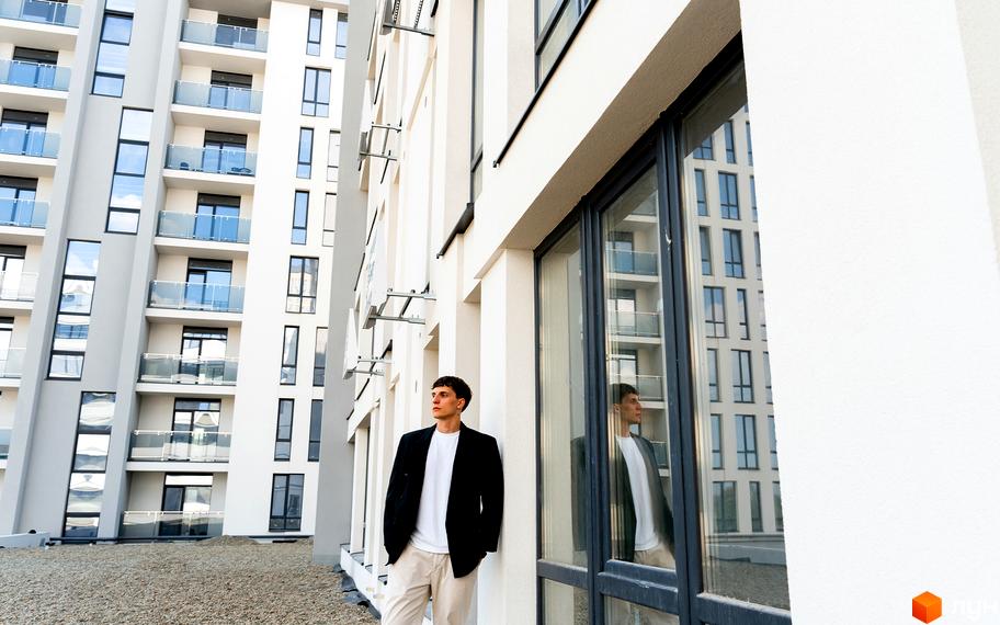 Житловий комплекс Kniahynyn-Center: фасад будівлі з балконами та вікнами, чоловік біля стіни, відображення у вікні.