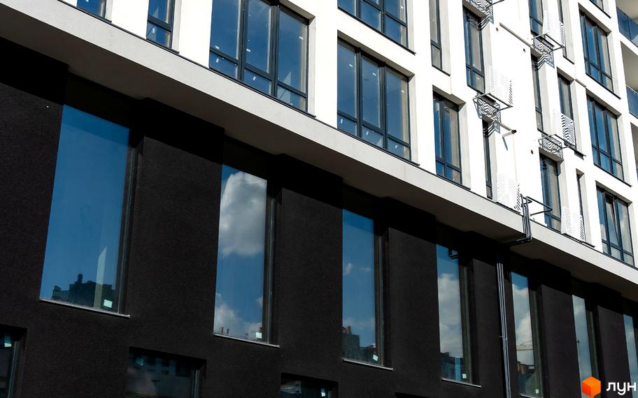 Фасад житлового комплексу Kniahynyn-Center з великими вікнами та чорними елементами. Зовнішній вигляд новобудови з відблисками неба та хмар у склі.