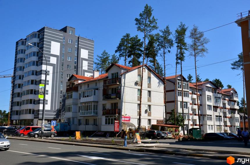 Новобудова на вулиці Університетська, 2ю. Багатоповерховий будинок сірого кольору з білими елементами та низькоповерхові будинки з червоними дахами.