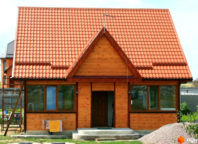 Котеджне містечко КМ Королівський сад: дерев'яний будинок з червоним черепичним дахом та великими вікнами. Поруч сходи, сушарка з одягом та насип гравію.