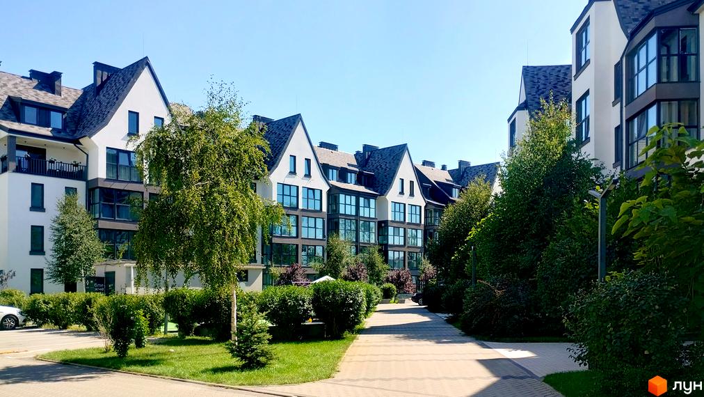 Житловий комплекс Desna Park Residence з білими фасадами та темними дахами, великими вікнами та доглянутою прибудинковою територією з деревами та кущами.