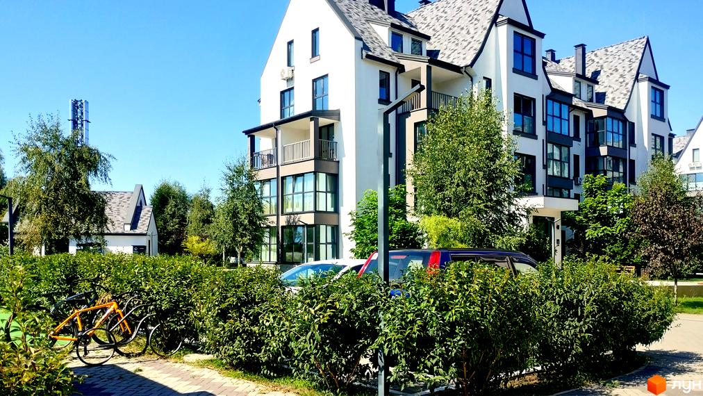 Житловий комплекс Desna Park Residence: біла багатоповерхова будівля з сірим дахом, балконами та великими вікнами, оточена зеленню та велосипедами.