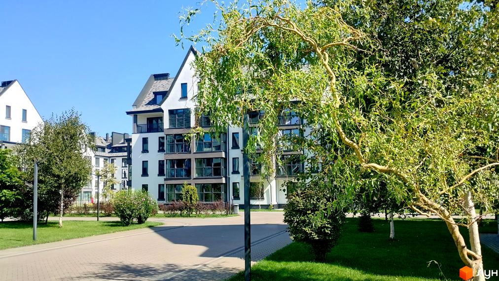 Житловий комплекс Desna Park Residence з білими фасадами та великими вікнами, оточений зеленою прибудинковою територією та деревами.