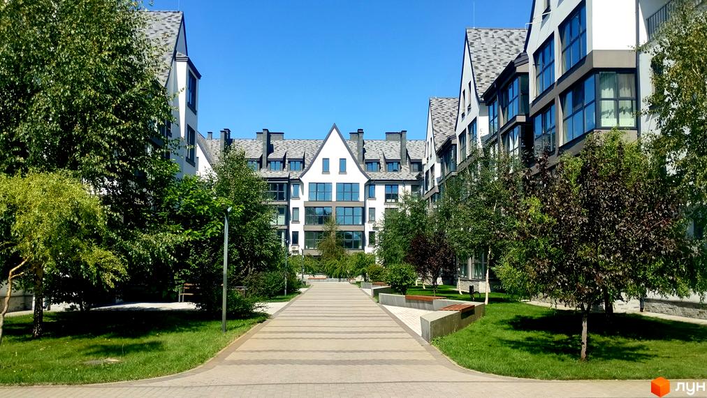 Новобудова Desna Park Residence з елегантними фасадами та великими вікнами, оточена доглянутою прибудинковою територією з зеленими насадженнями та пішохідною алеєю.