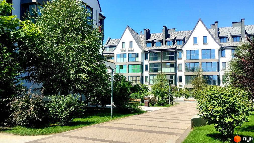 Зовнішній вигляд будинків ЖК Desna Park Residence з великими вікнами та доглянутою прибудинковою територією з зеленими насадженнями та доріжками.