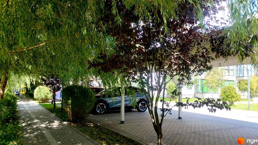 Житловий комплекс Desna Park Residence з автомобілем під навісом та доглянутою прибудинковою територією з деревами та пішохідною доріжкою.