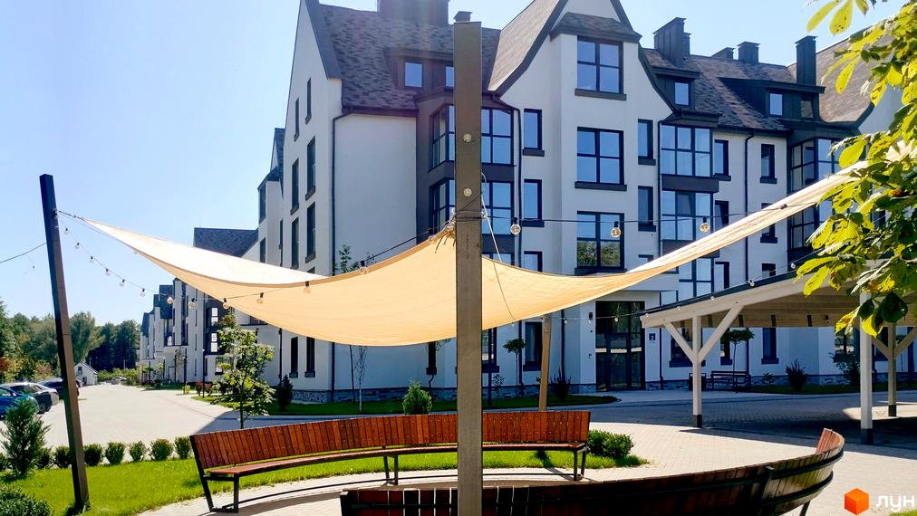 Зовнішній вигляд будинків житлового комплексу Desna Park Residence з навісом та лавками на прибудинковій території.
