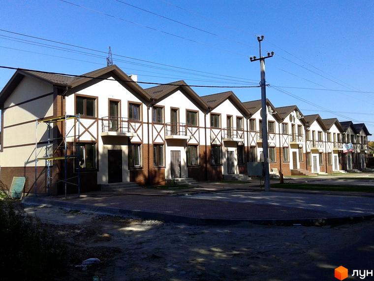 Зовнішній вигляд таунхаусів на вулиці Садова, 77. Фасади оздоблені світлою штукатуркою та коричневими дерев'яними елементами. Перед будинками облаштований бруківкою двір.