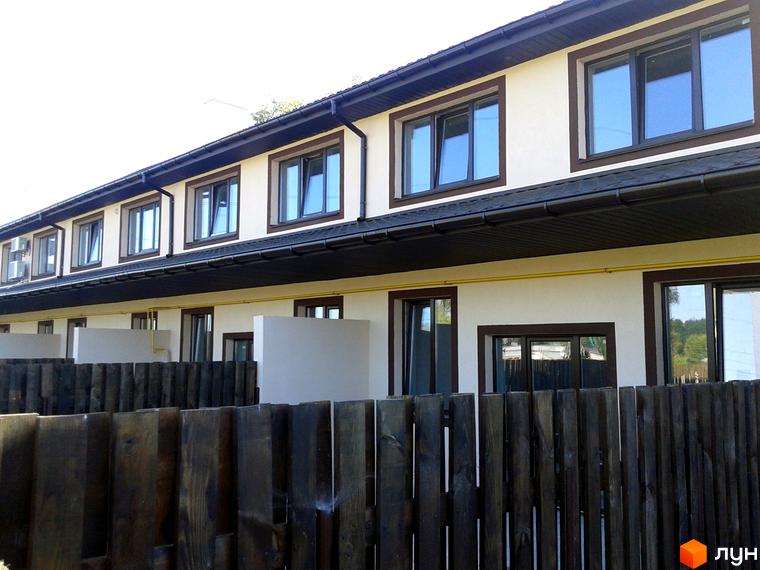 Зовнішній вигляд новобудови на вул. Садова, 77. Фасад будинку світлий, вікна темні. Перед будинком дерев'яний паркан.