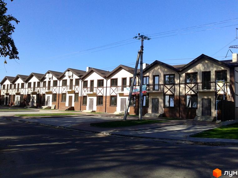 Новобудова на вул. Садова, 77. Будинки з білою та коричневою обробкою, з балконами та темними вікнами, розташовані вздовж дороги з зеленою зоною.