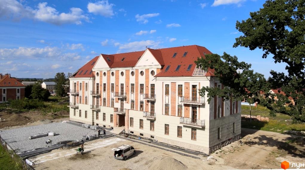 Зовнішній вигляд будинку ЖК Австрійський з червоним дахом та балконами, поруч будівельний майданчик з технікою та матеріалами. Дізнайтесь про новобудову на нашому сайті.