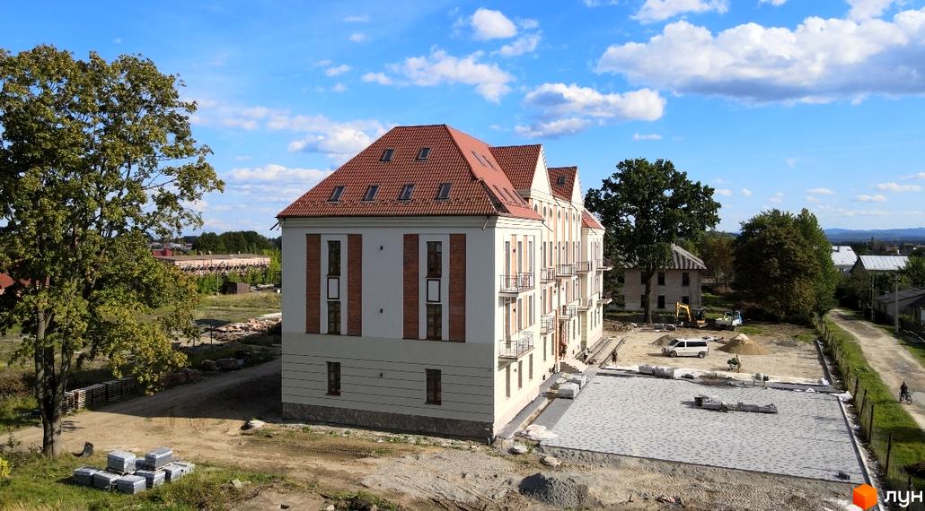 Будівельний проєкт ЖК Австрійський з червоним дахом та балконами. На прибудинковій території видно будівельні матеріали та техніку.