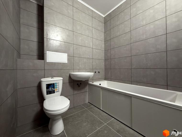 Сучасний санвузол з білою ванною, унітазом та раковиною, оздоблений сірою плиткою. ЖК Центр – це комфортне житло у розвиненому районі.