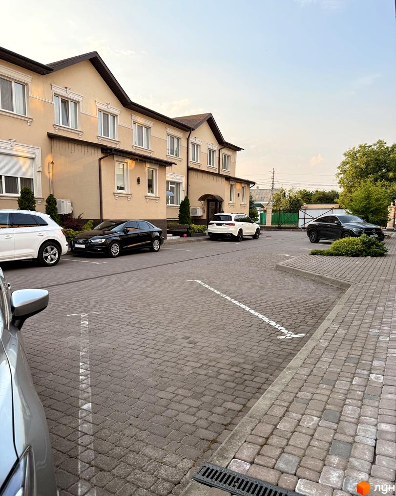 Зовнішній вигляд житлового комплексу Cappuccino House з паркуванням та автомобілями. Навколо будівлі облаштована прибудинкова територія.