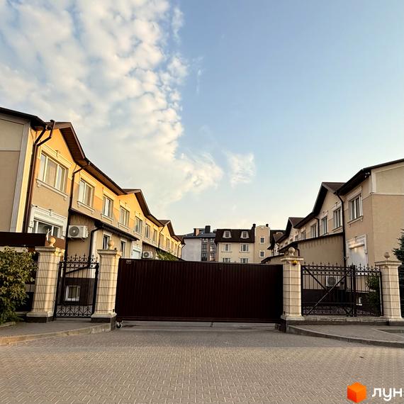 Зовнішній вигляд будинків ЖК Cappucсino House з брамою та парканом. Навколо розташовані зелені насадження та бруківка.