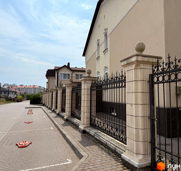 Фасад будинку ЖК Cappucсino House з кованим парканом та колонами. Поруч розташована парковка з обмежувачами.