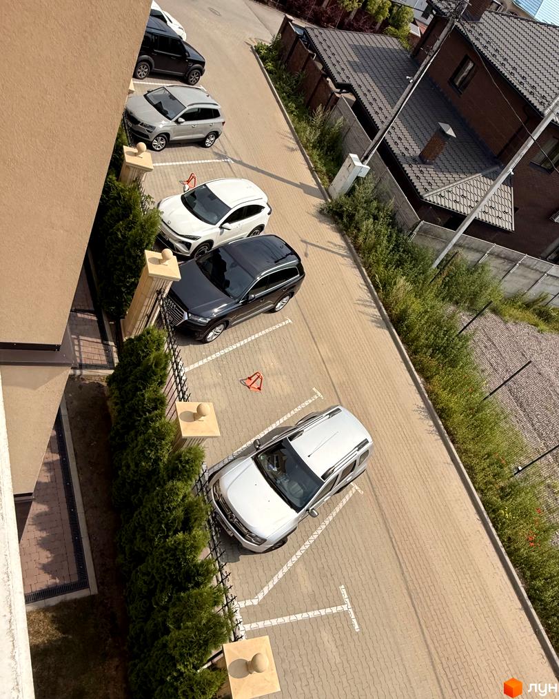 Новобудова ЖК Cappucсino House з парковкою та зеленими насадженнями. На зображенні видно автомобілі, припарковані біля будинку.