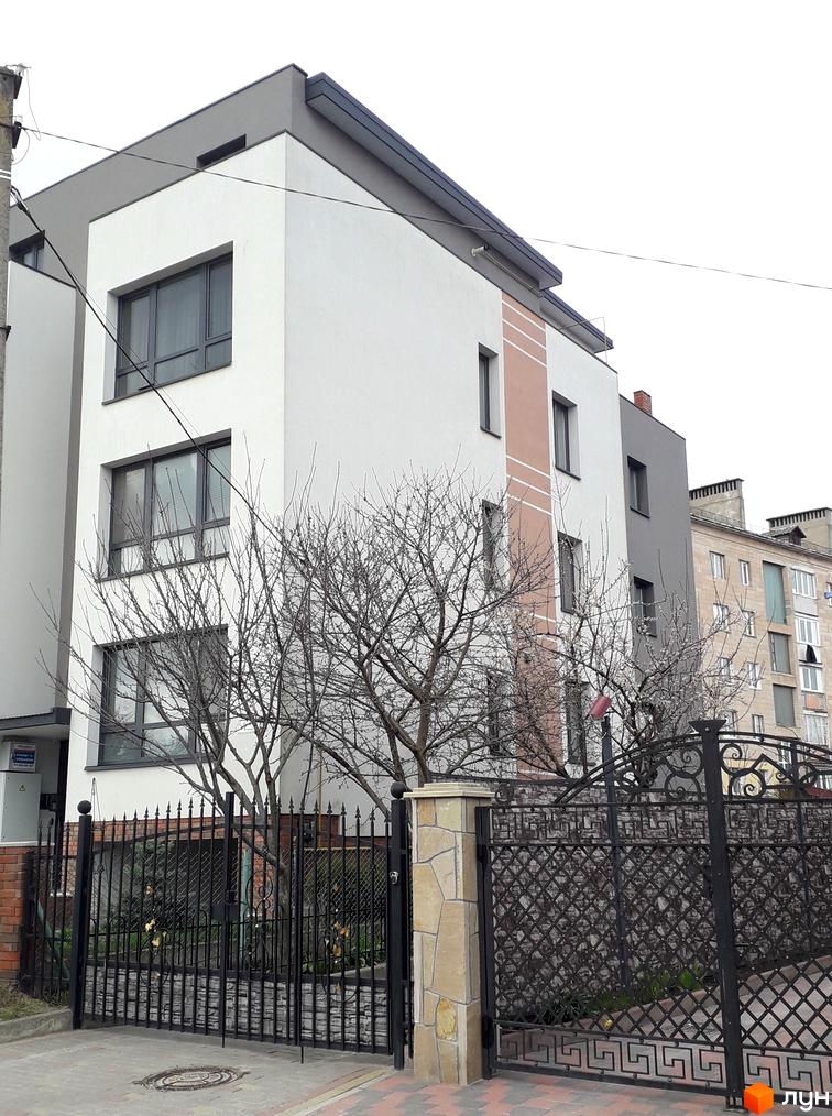 Фасад житлового комплексу на вул. Назарія Яремчука, 42, з кованою огорожею та деревами перед будинком. Зовнішній вигляд новобудови з сірими та білими елементами.