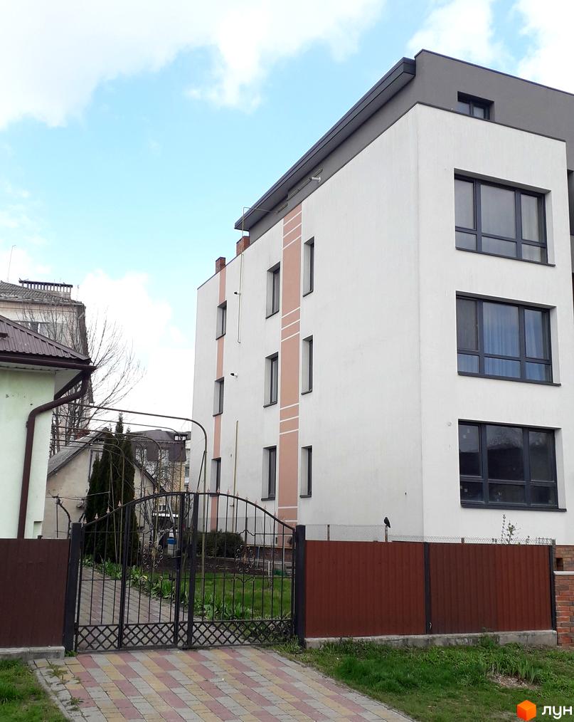 Фасад новобудови на вул. Назарія Яремчука, 42, з великими вікнами та декоративними елементами. Перед будинком розташований кований паркан та доглянута прибудинкова територія.