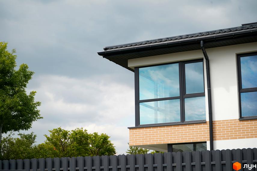 Квадрекс Quattro - новобудова з великими вікнами та цегляним фасадом. Навколо будинку зелені дерева та сітчастий паркан.