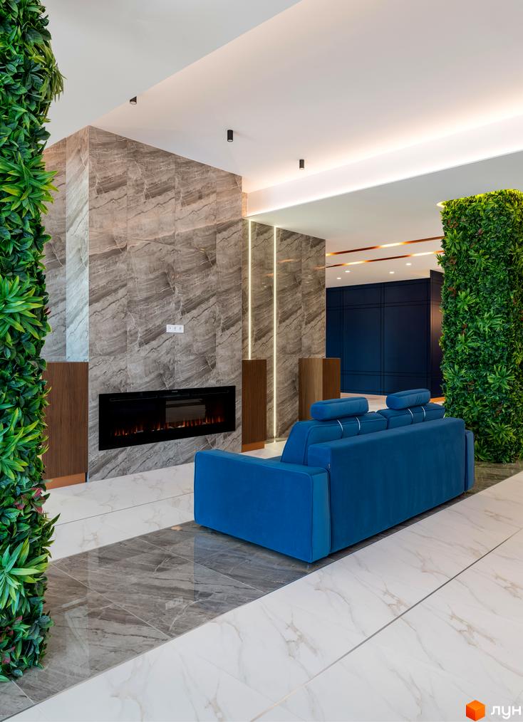 Інтер'єр вітальні в ЖК Edelweiss House з каміном, синім диваном та вертикальним озелененням. Сучасний дизайн простору з мармуровою плиткою та прихованим освітленням.