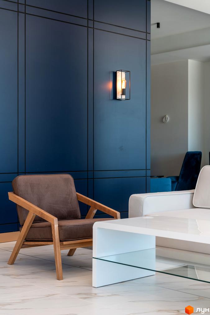 Інтер'єр вітальні ЖК Edelweiss House з коричневим кріслом та білим диваном. Сучасні меблі та оздоблення створюють затишну атмосферу.