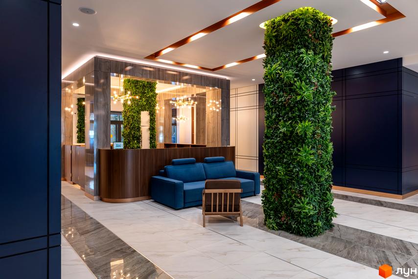 Інтер'єр холу житлового комплексу Edelweiss House з диваном, кріслом та вертикальним озелененням.