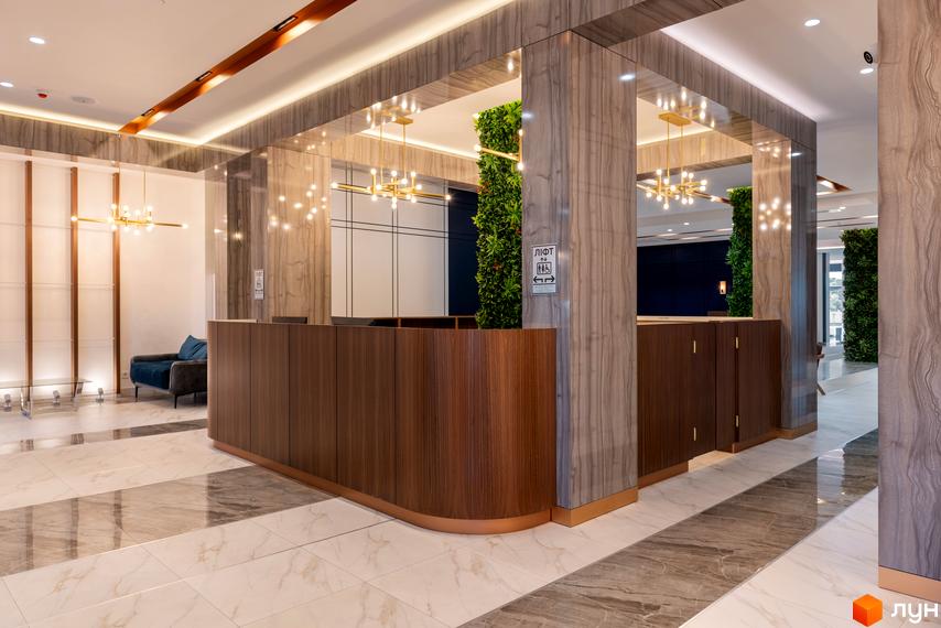 Сучасний хол житлового комплексу Edelweiss House з ресепшн, диваном та вертикальним озелененням. Оздоблення стін та підлоги мармуром та деревом.
