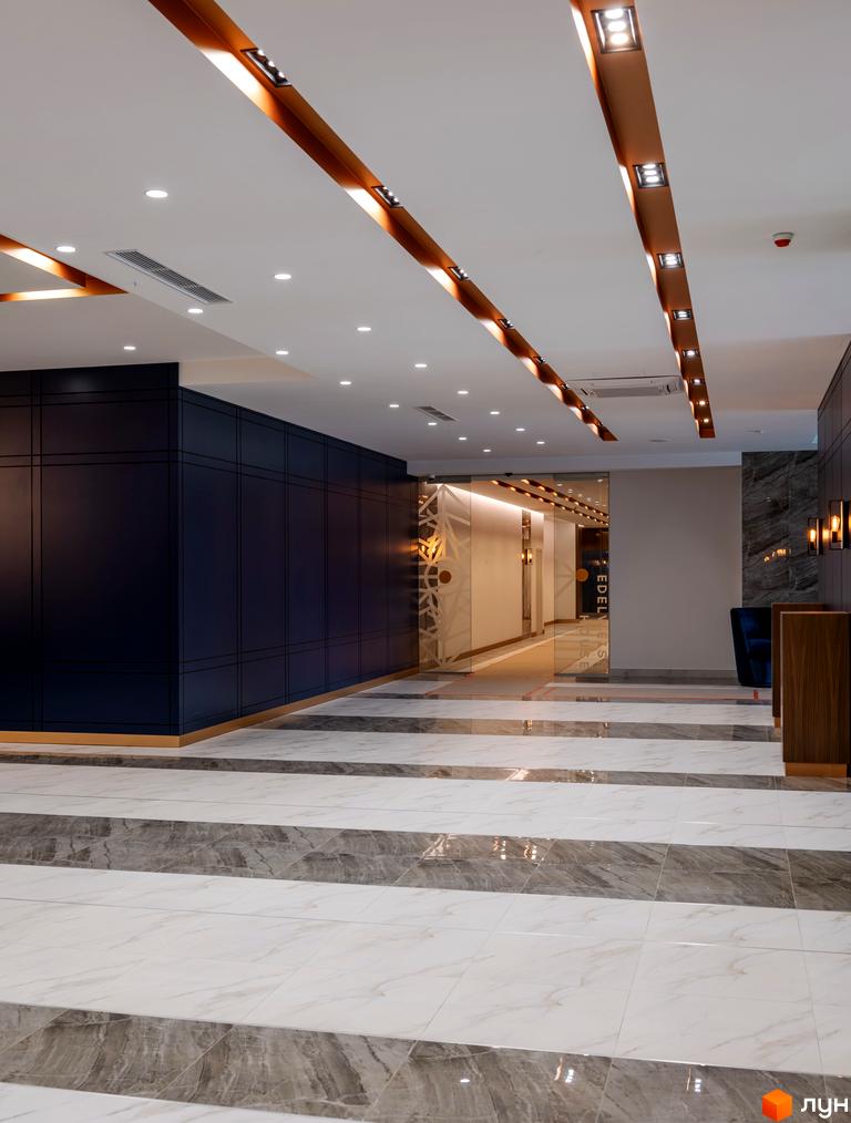 Сучасний інтер'єр холу новобудови ЖК Edelweiss House з мармуровою підлогою та стильним освітленням. Опис просторого та елегантного входу до житлового комплексу.