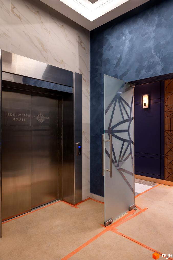 Сучасний вхід до житлового комплексу Edelweiss House з елегантними дверима та оздобленням стін. Фото інтер'єру новобудови.