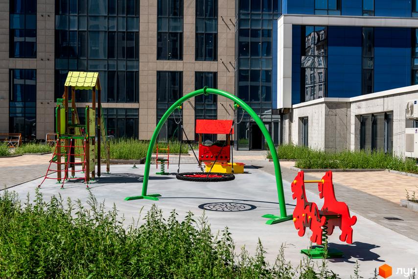 Дитячий майданчик біля новобудови ЖК Edelweiss House із зеленими гойдалками та гірками. Сучасний житловий комплекс з елементами благоустрою.