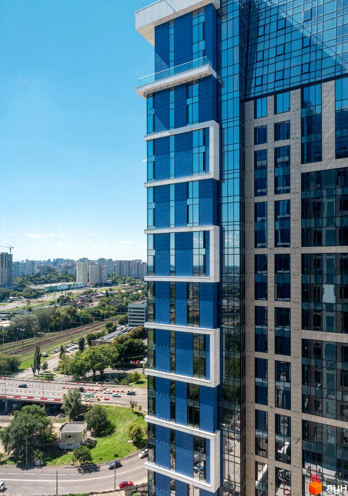 Житловий комплекс Edelweiss House з блакитними та сірими фасадами, що височіє над міським пейзажем з дорогою та залізницею.