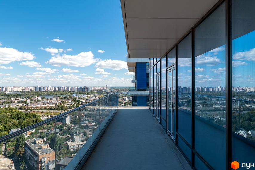 Вид з балкона на місто з новобудови ЖК Edelweiss House. Панорамні вікна та скляні огородження балкона відкривають вид на міський пейзаж та хмари.