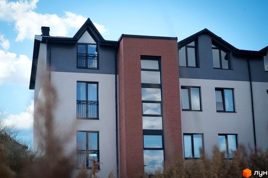 Зовнішній вигляд новобудови ЖК Амстердам з цегляною вставкою та великими вікнами. Будинок має сіро-білий фасад та темний дах.