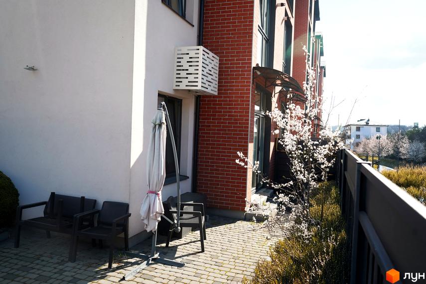 Житловий комплекс Амстердам з цегляним фасадом та затишною прибудинковою територією з кріслами та парасолькою.