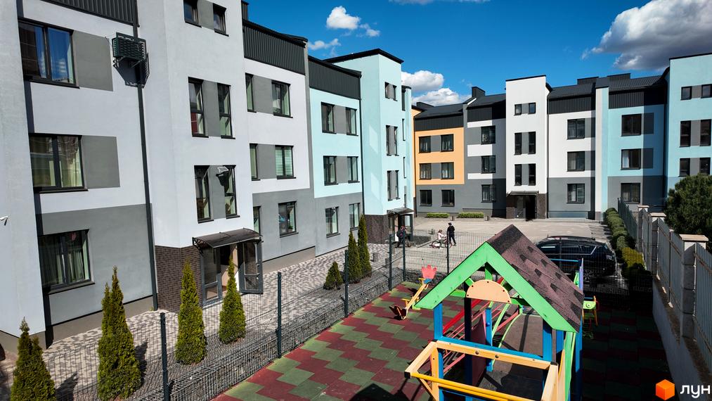 Житловий комплекс Вілла Італія: фасади будинків у світло-сірих та блакитних тонах, прибудинкова територія з дитячим майданчиком та зеленими насадженнями.