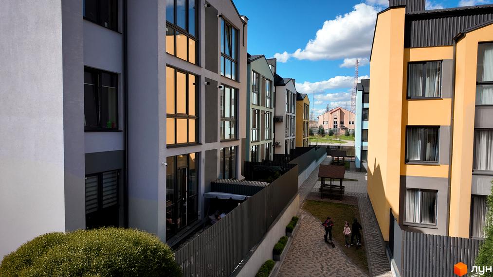 Житловий комплекс Вілла Італія. Фасади будівель виконані в світлих тонах з великими вікнами. Поруч розташована прибудинкова територія з доріжками та зонами відпочинку.