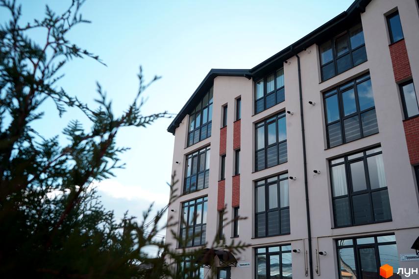 Фасад житлового комплексу Грушевського, 3а, з великими вікнами та цегляними вставками на тлі блакитного неба.