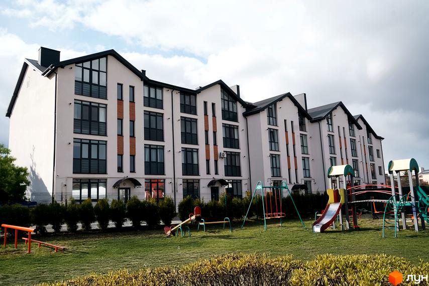 Новобудова ЖК Грушевського з великою кількістю вікон та дитячим майданчиком поруч. Зовнішній вигляд будинку та прибудинкова територія.