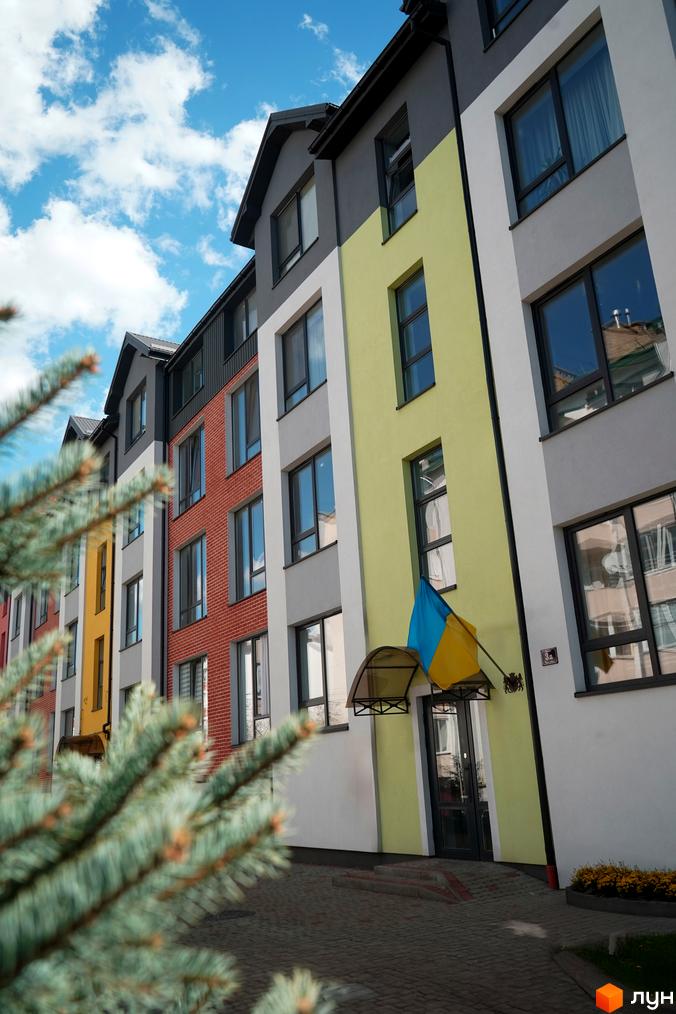 Житловий комплекс Флоренція: фасади будівель з різнокольоровими елементами та українським прапором, прибудинкова територія з бруківкою та зеленню.