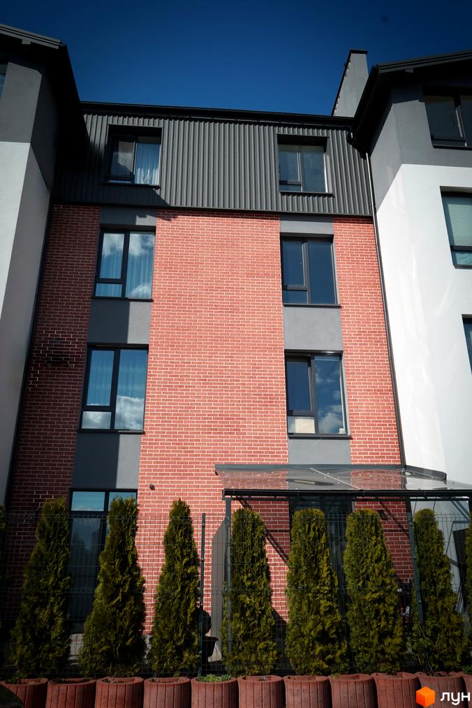 Житловий комплекс Флоренція: фасади з червоної цегли та сірих панелей, вікна з відображенням хмар, зелені туї біля паркану.