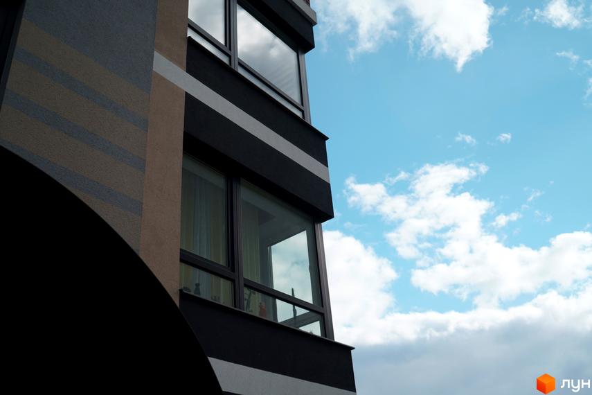 Будинок ЖК Вілла Венеція з панорамними вікнами на тлі блакитного неба з хмарами. Зовнішній вигляд фасаду з декоративними смугами.