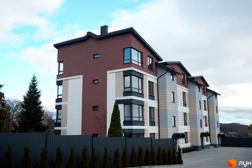 Житловий комплекс Вілла Венеція - це сучасна новобудова з цегляним фасадом та великими вікнами. Територія навколо будинку огороджена парканом, а перед ним висаджені туї.