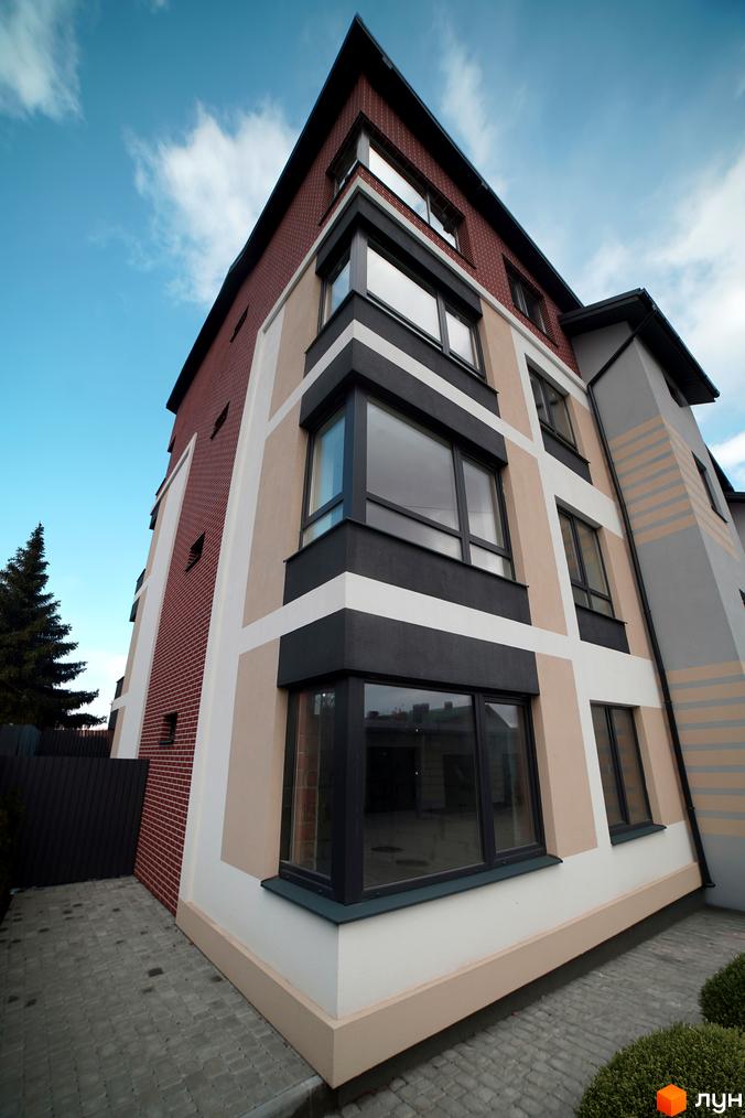 Житловий комплекс Вілла Венеція. Зовнішній вигляд будинку з червоної цегли та бежевими елементами, вікна з темними рамами. Прибудинкова територія вимощена плиткою.