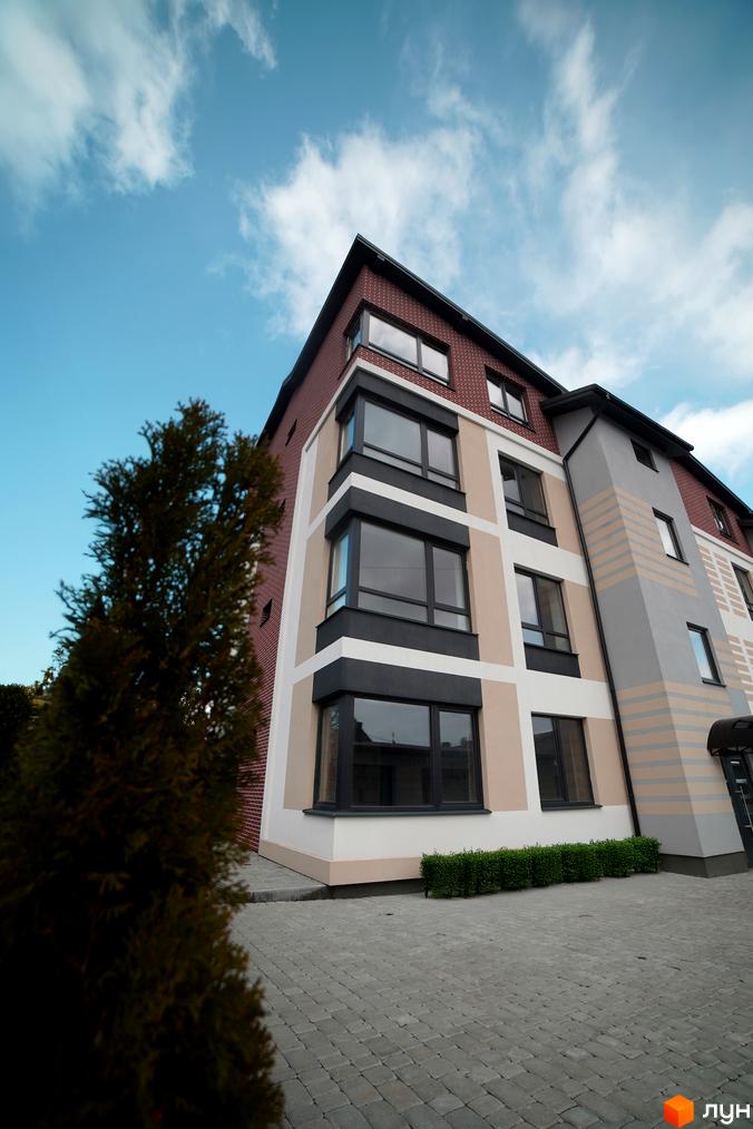 Зовнішній вигляд новобудови ЖК Вілла Венеція з цегляним фасадом та великими вікнами. Прибудинкова територія викладена бруківкою.