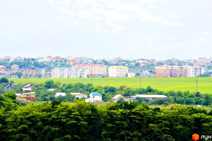 Багатоповерхові будинки Житлового комплексу Озерки з різнокольоровими фасадами на тлі зелених полів та приватної забудови.