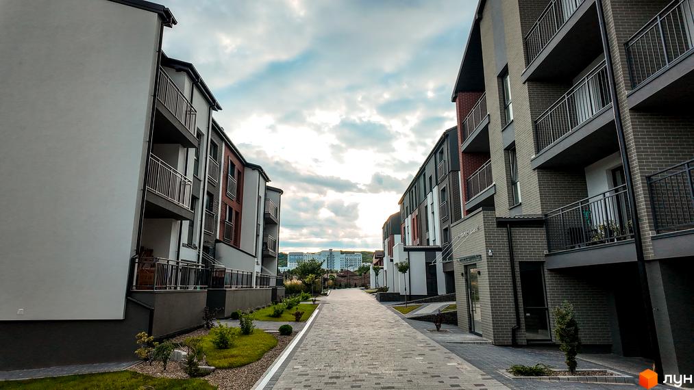 Житловий комплекс Вілла Швейцарія. Сучасні будівлі з балконами та бруківкою, що веде до них. Навколо зелені насадження та дерева.