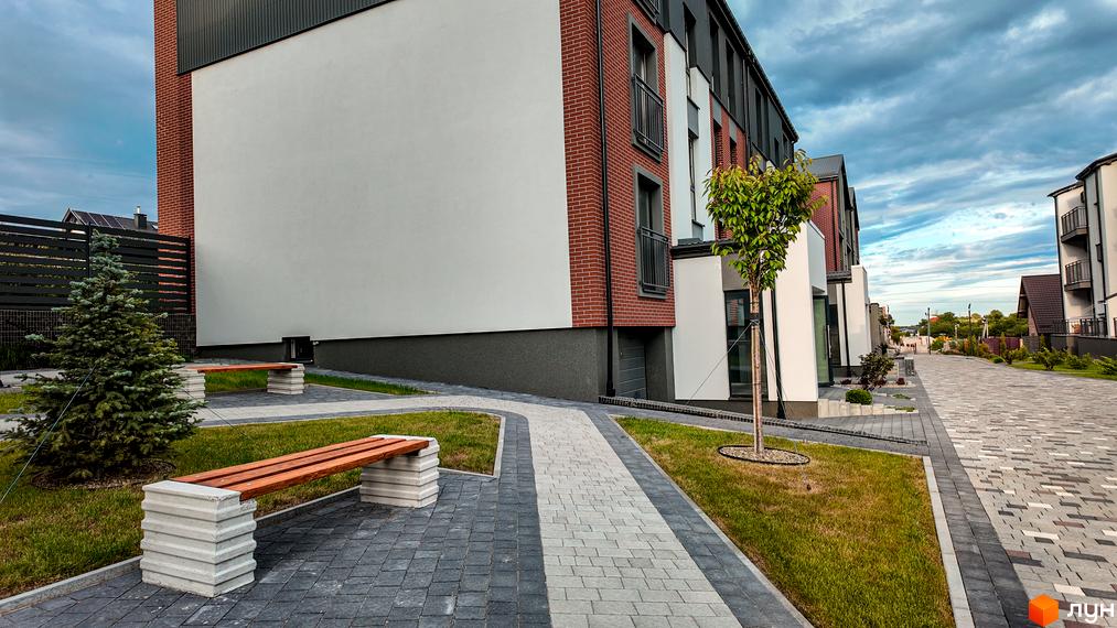 Житловий комплекс Вілла Швейцарія. Зовнішній вигляд будівель з цегляним фасадом та білими вставками. Прибудинкова територія з доріжками та зеленими насадженнями.